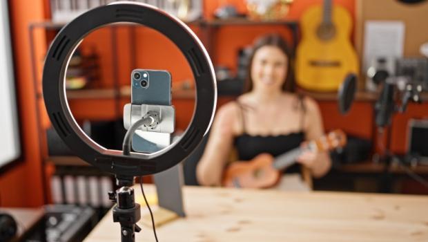 A woman playing the ukulele and recording herself with a phone and ring light