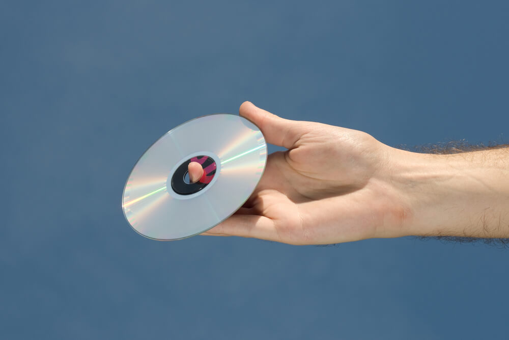 A hand holds a CD against a blue sky.