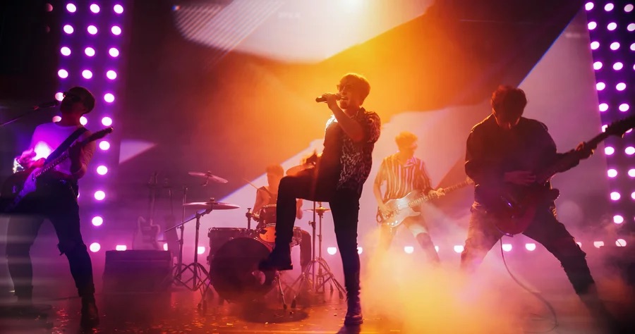 A rock band performs on stage under orange and purple lights.